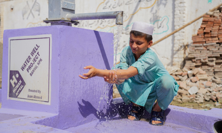 Boy washing his arms with a water well pump