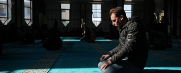 Man preparing to pray in a masjid, framed by light from a window