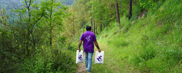 Human Appeal staff member walking down a forested path, carrying two bags of Qurbani to deliver them