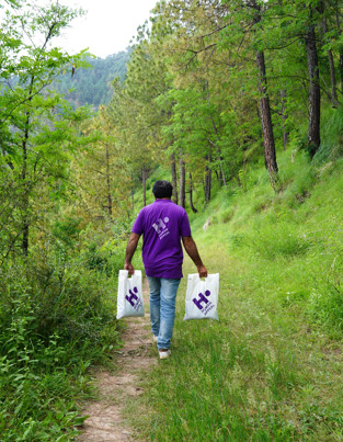 Human Appeal staff member walking down a forested path, carrying two bags of Qurbani to deliver them