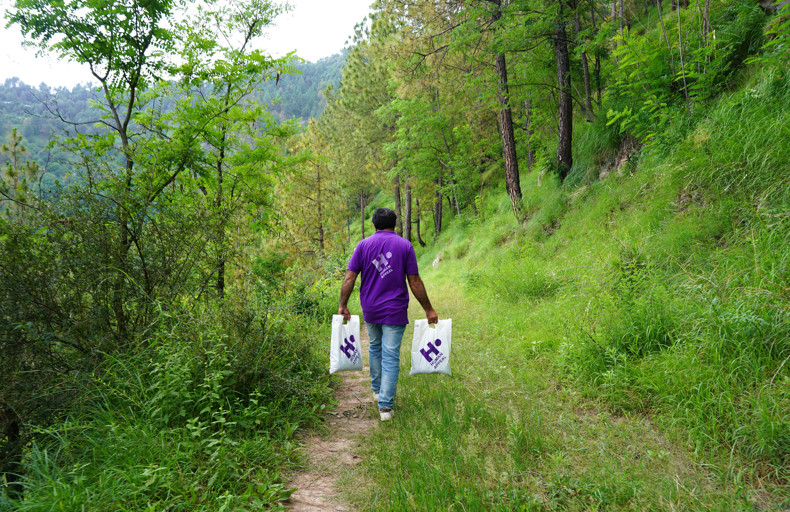 Human Appeal staff member walking down a forested path, carrying two bags of Qurbani to deliver them