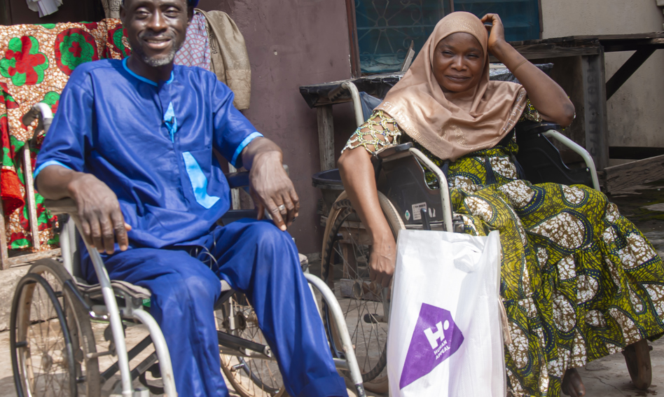 Two people in wheelchairs, a Qurbani bag between them