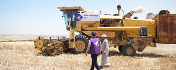 Human Appeal staff walking with a farmer, next to mechanical farming equipment