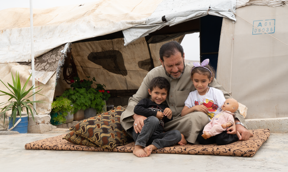 Father with his children, sitting on a rug outside the tent
