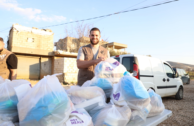 Man standing behind a bundle of bagged hot meals