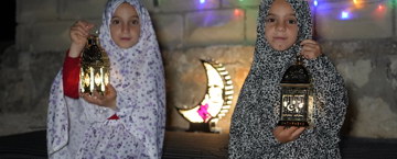 A pair of girls sitting down, holding lanterns at night
