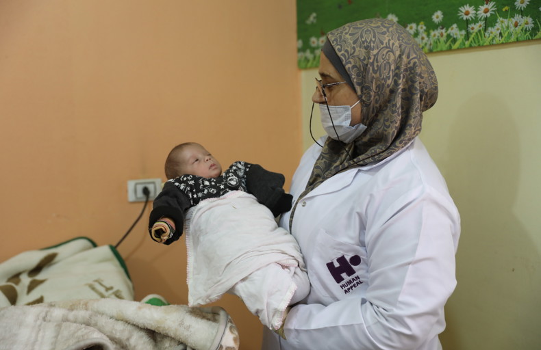 Newborn baby held up by a medical professional in Al Iman