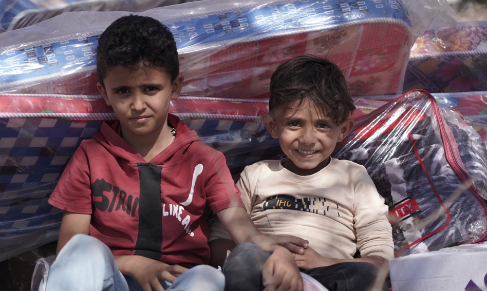 Two children leaning against a stack of bagged mattresses